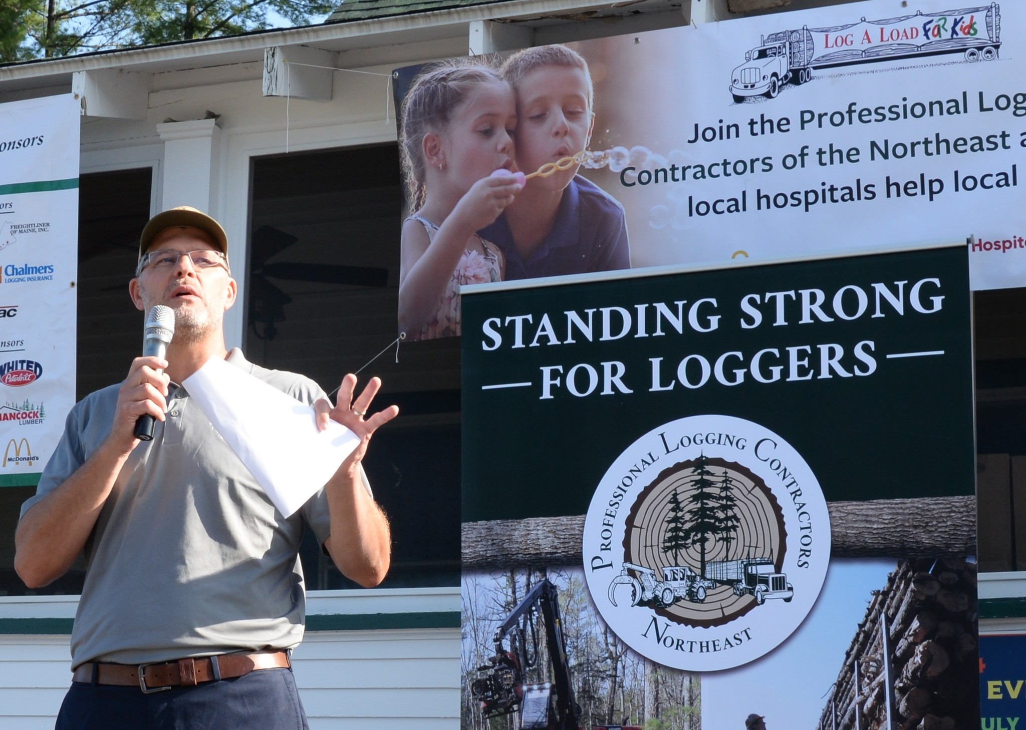 photo of PLC Executive Director Dana Doran standing in front a building and banners speaking to a crowd while holding a microphone