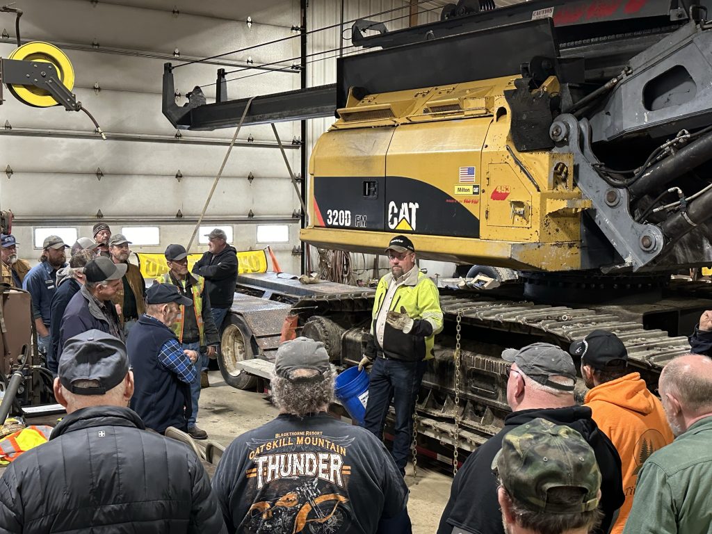 photo of a man standing in front of a large piece of forestry equipment speaking to a group people during PLC's annual logger and fleet safety training series