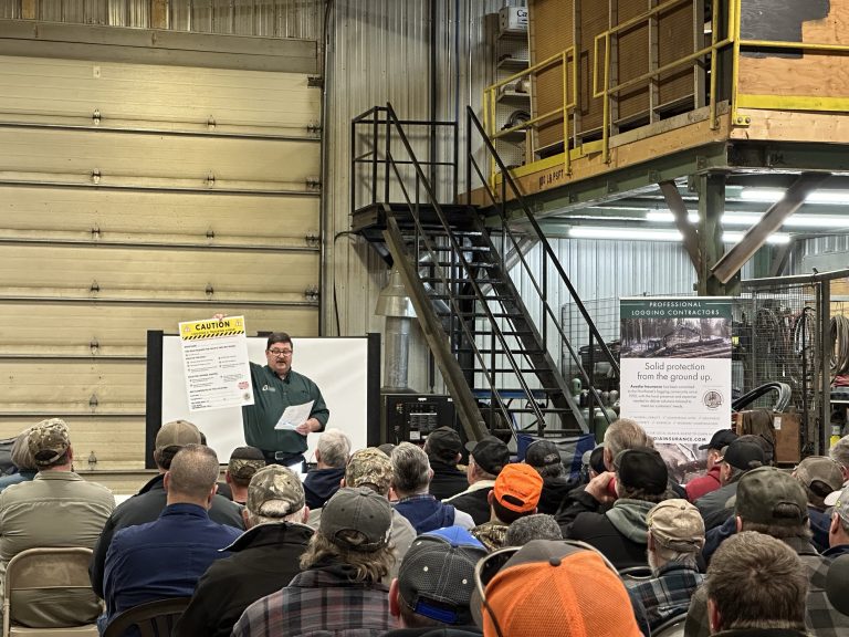 photo of a man holding a poster that reads caution in front of a group of people in a warehouse at a safety training meeting