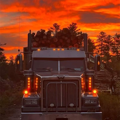 photo of a logging truck filled with logs with a red sunset in the background