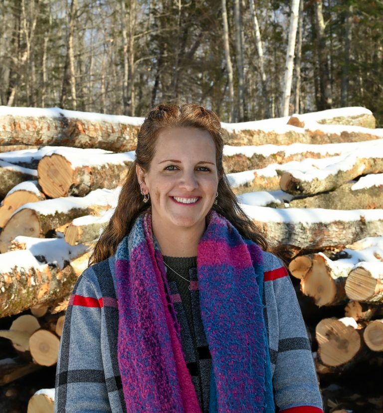 Brown haired woman standing in front of a pile of logs