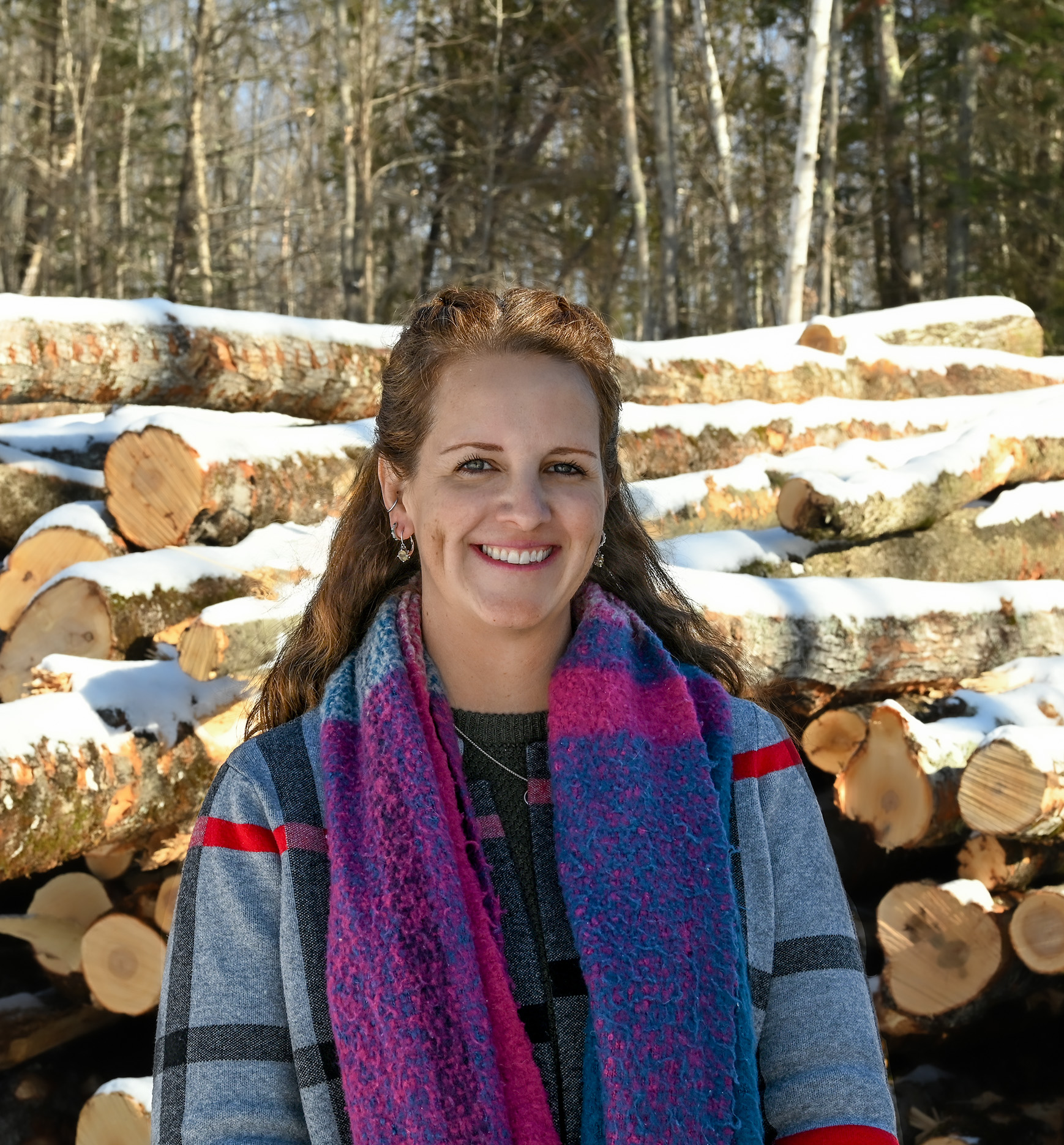 Brown haired woman standing in front of a pile of logs